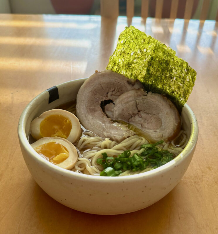 Made By Jerwat's personalized ramen bowl with pork belly, a marinated egg, dried seaweed and chopped green onions.